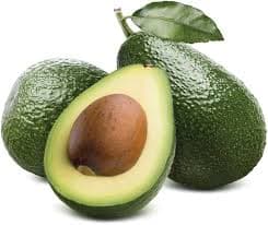 Halved avocado showing smooth green flesh and a pit, placed on a rustic surface with whole fruits nearby.